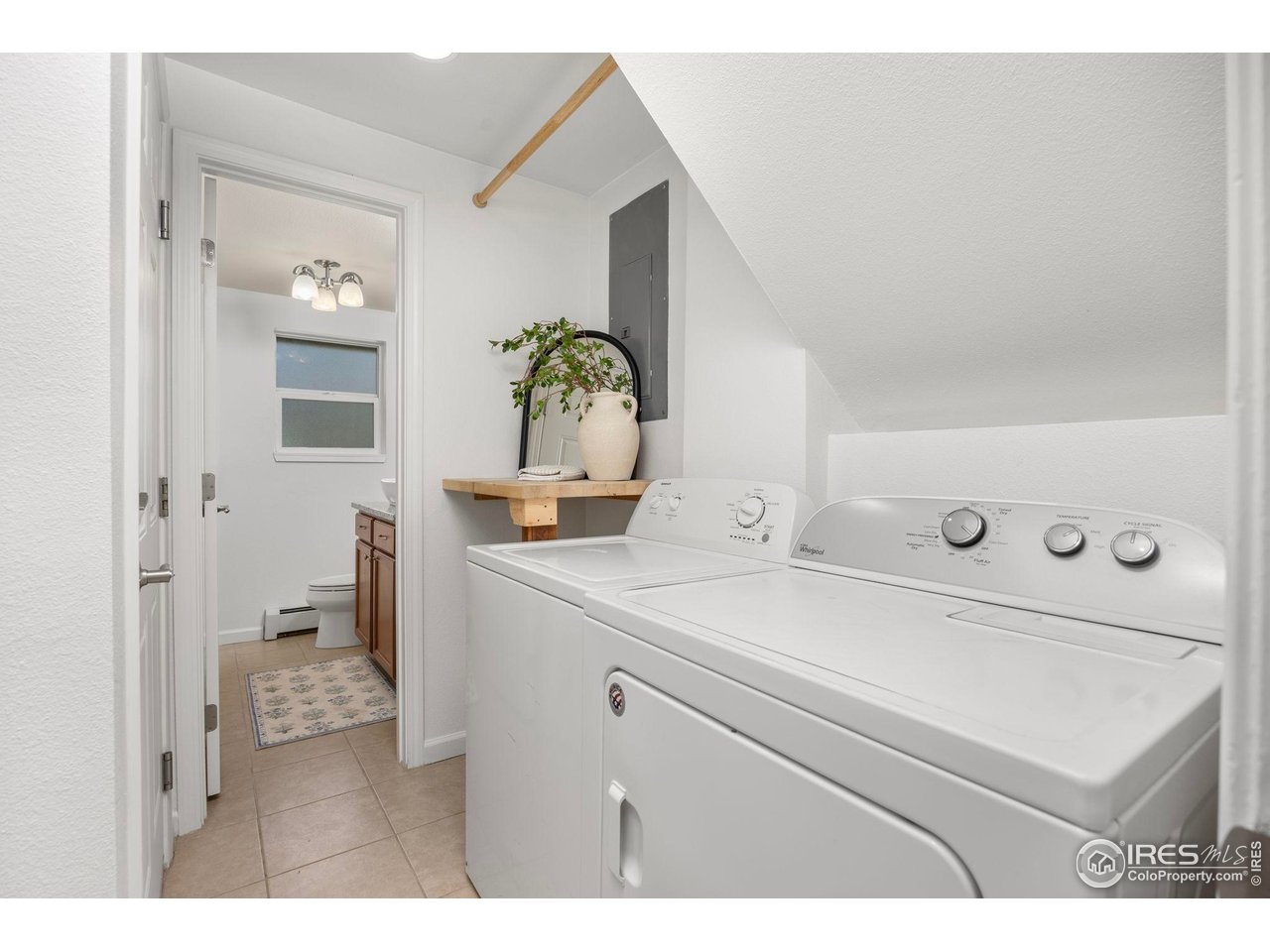 Laundry room with white washer and dryer, wooden folding shelf, and bathroom visible through the doorway.