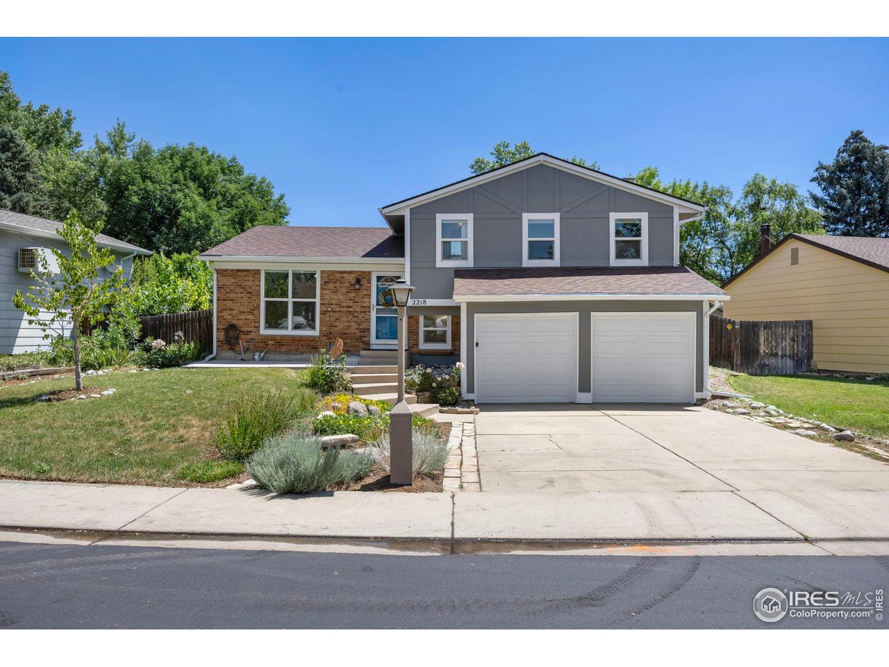 Two-story gray and brick home with a blue front door, double garage, and landscaped yard.