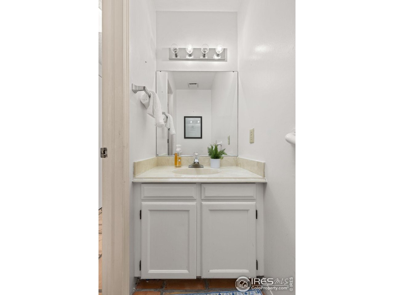 Bathroom vanity with a large mirror, four-light fixture, and white cabinet.