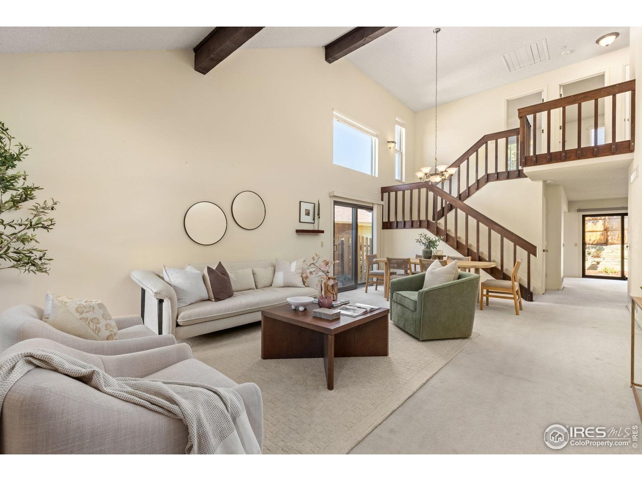 Staged living room with vaulted ceilings, exposed beams, and a dark wood staircase leading to a loft.