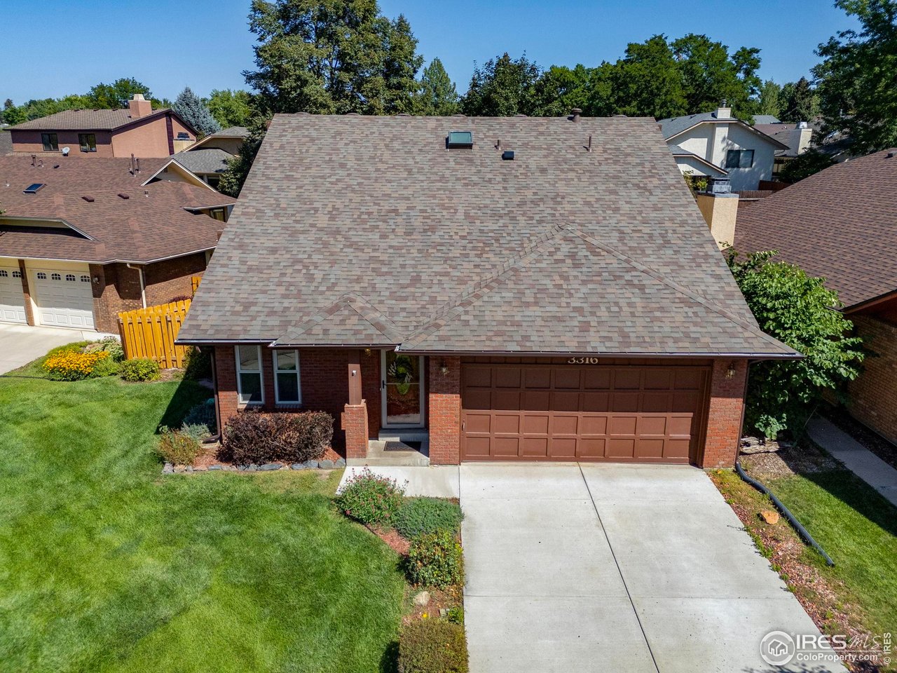Brick home with a broad shingle roof, attached two-car garage, and landscaped front lawn.