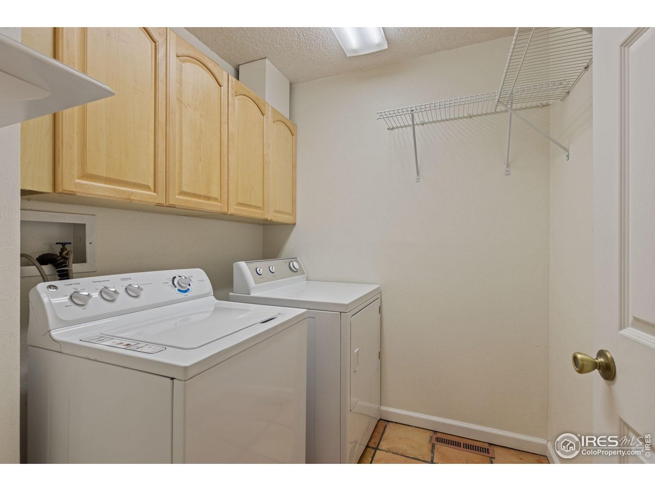 Laundry room with a washer and dryer beneath light wood cabinets and a wire shelf.