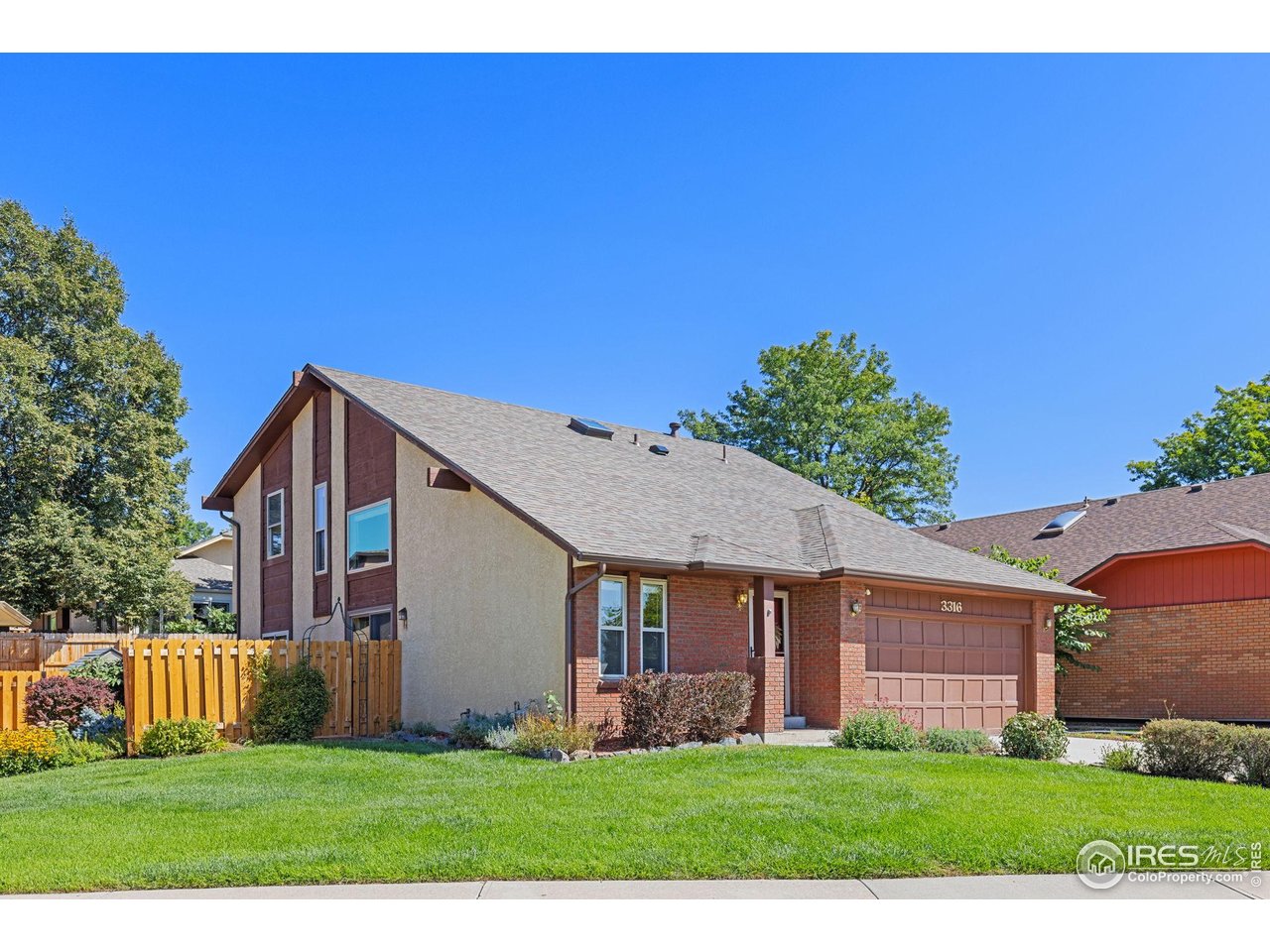 Two-story brick and tan home with a double garage and fenced green lawn.