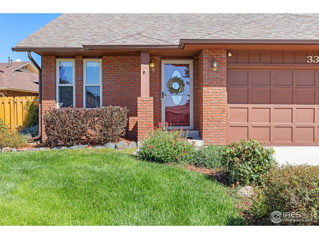 Brick home exterior with an attached garage, wreath-decorated front door, and flowering shrubs along the lawn.
