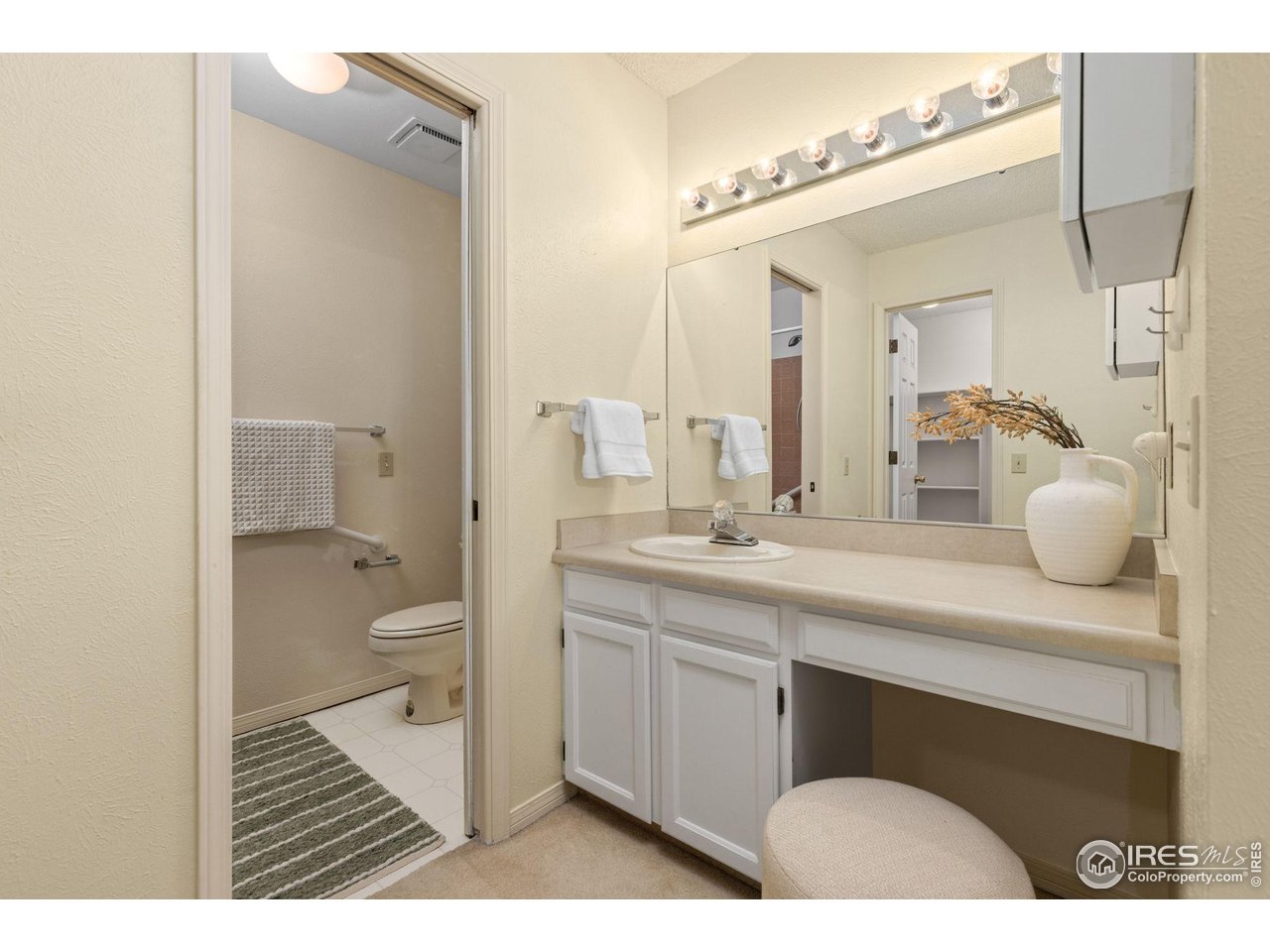Bathroom with a long white vanity and mirror, opening to a separate toilet area.