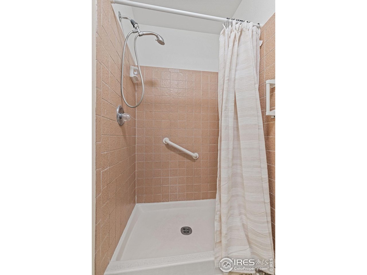 Tiled bathroom shower with a white curtain, handheld showerhead, and grab bars.