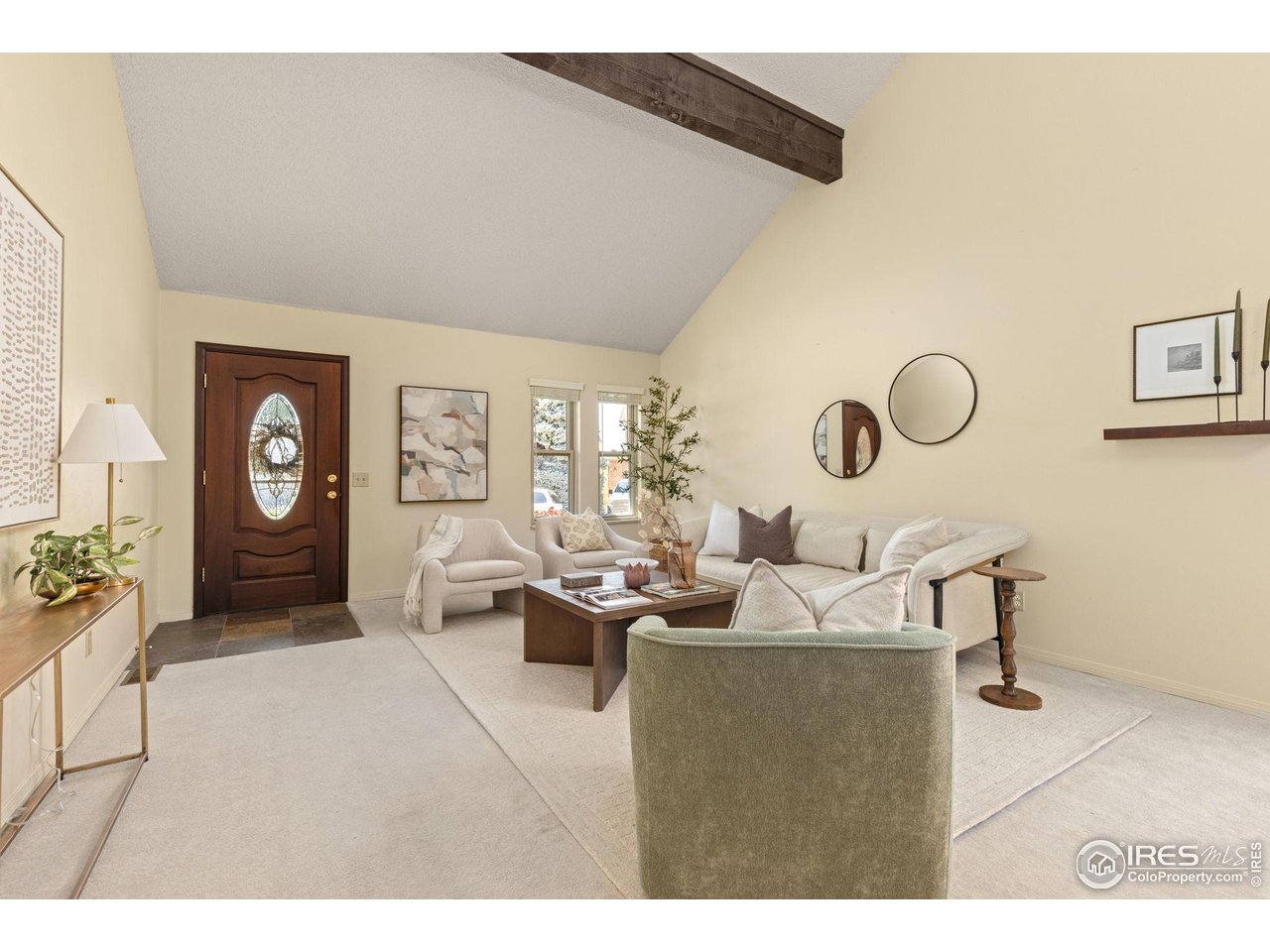 Staged living room with a vaulted ceiling, exposed wood beam, and oval-glass front door.