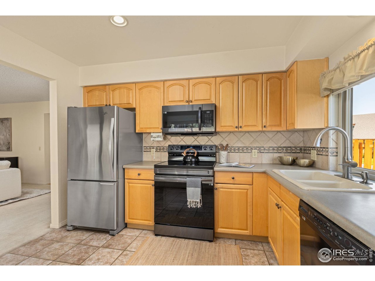 Kitchen with honey-colored cabinets, stainless appliances, and a double-basin sink beneath a window.