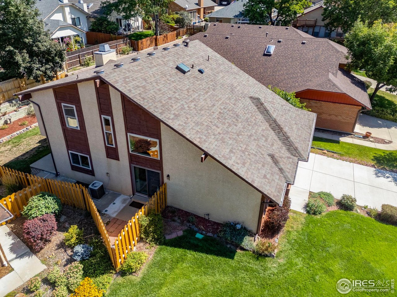 Aerial view of a two-story home with a broad shingled roof and fenced, landscaped yard.