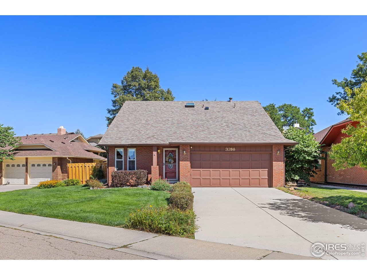 Brick house with a steep roof, two-car garage, and landscaped front lawn.
