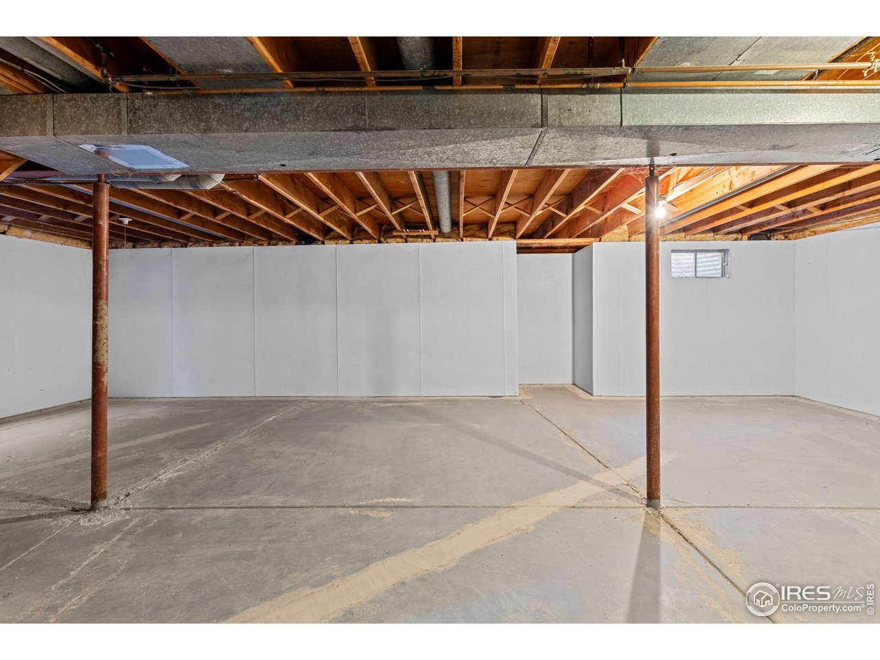 Unfinished basement with exposed ceiling joists, concrete floor, and two metal support posts.