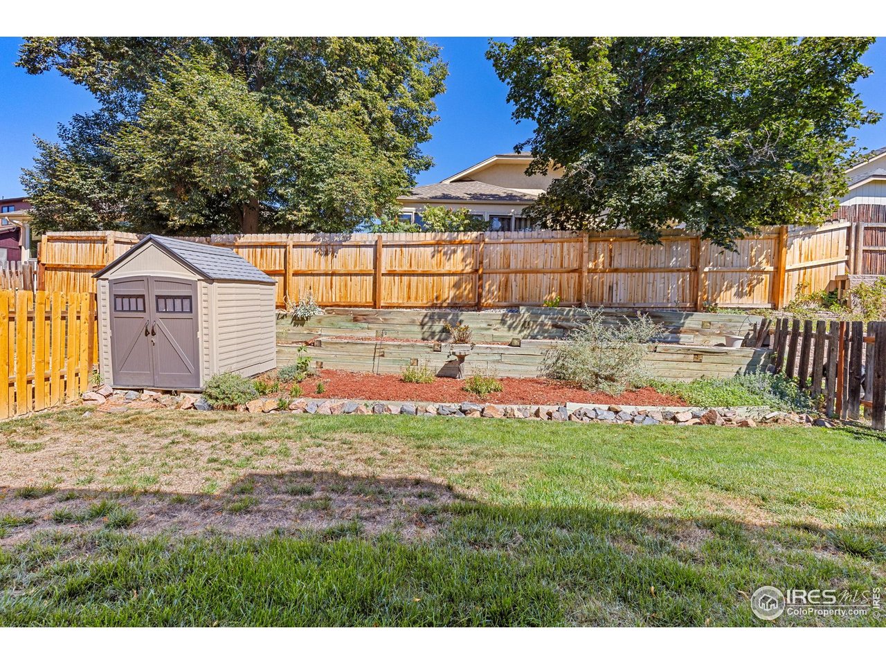 Fenced backyard with a storage shed, raised garden beds, and mature trees.