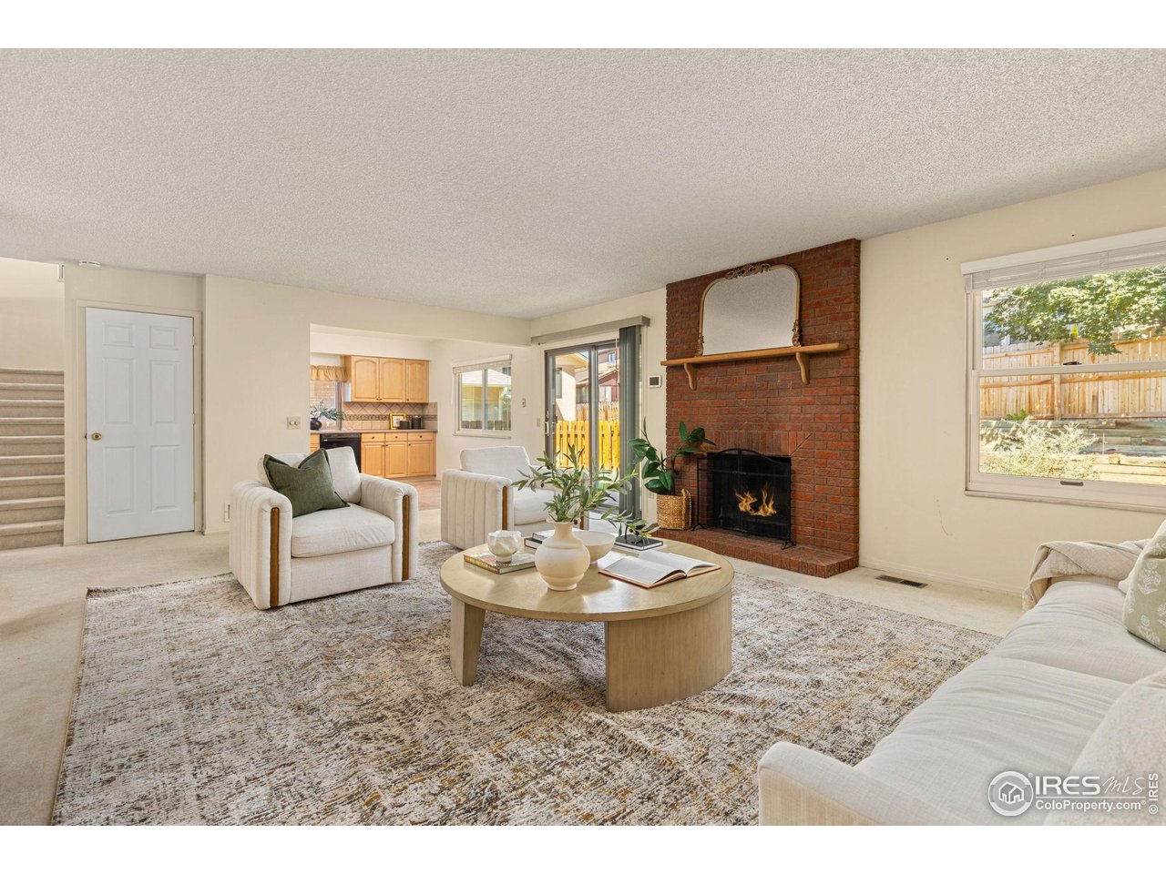Living room with a brick fireplace, neutral seating, and an open view into the kitchen.