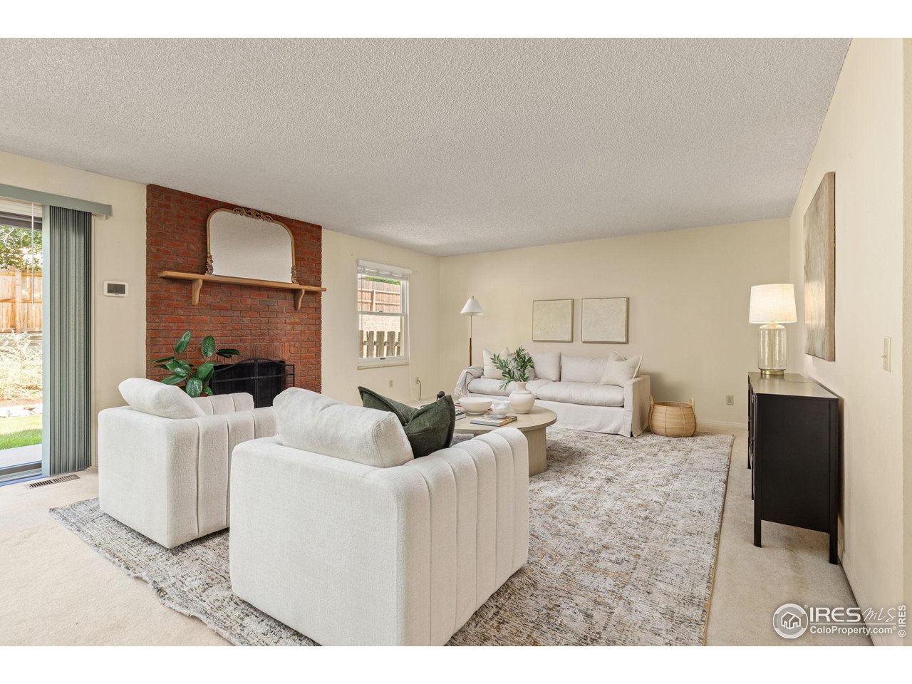 Living room with white sofas, a brick fireplace, and a large patterned rug.