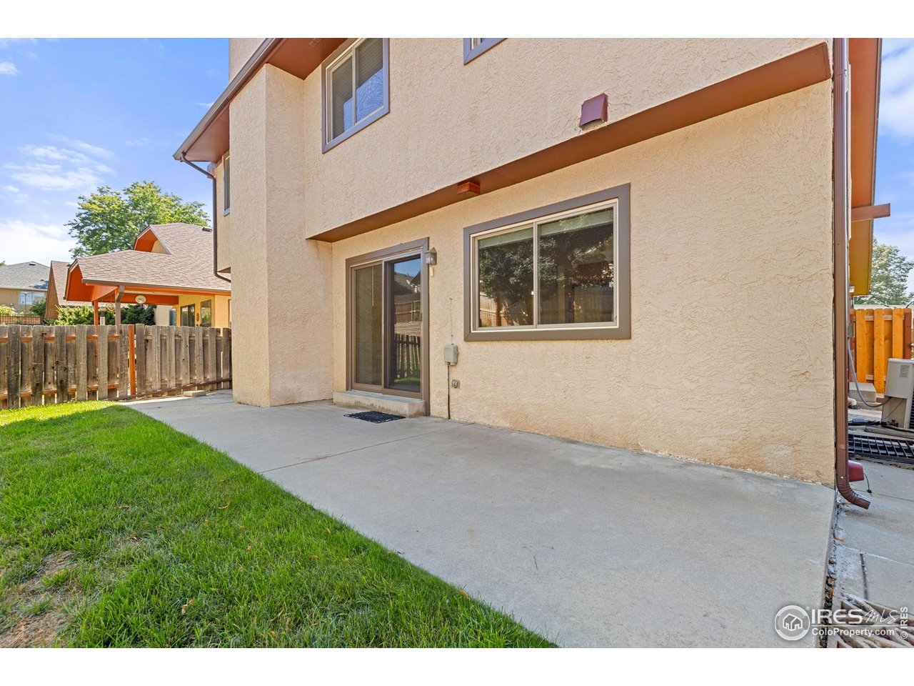 Rear patio of a beige stucco home with a concrete patio, lawn, and wooden privacy fence.
