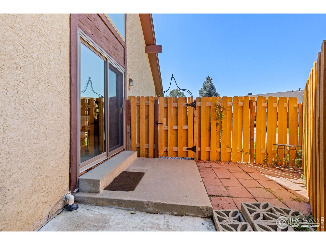 Fenced patio beside a stucco home, with a sliding glass door and red paver flooring.