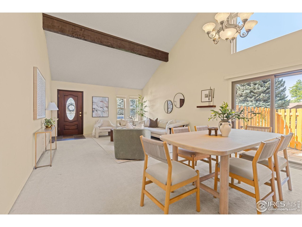 Open living and dining room with a vaulted ceiling, exposed beam, and sliding doors to a fenced patio.