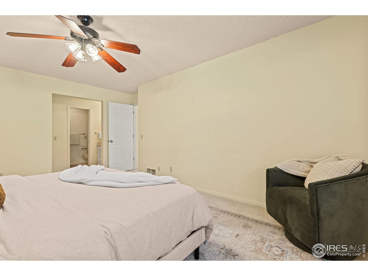 Bedroom with pale bedding, a dark chair, patterned rug, and ceiling fan.