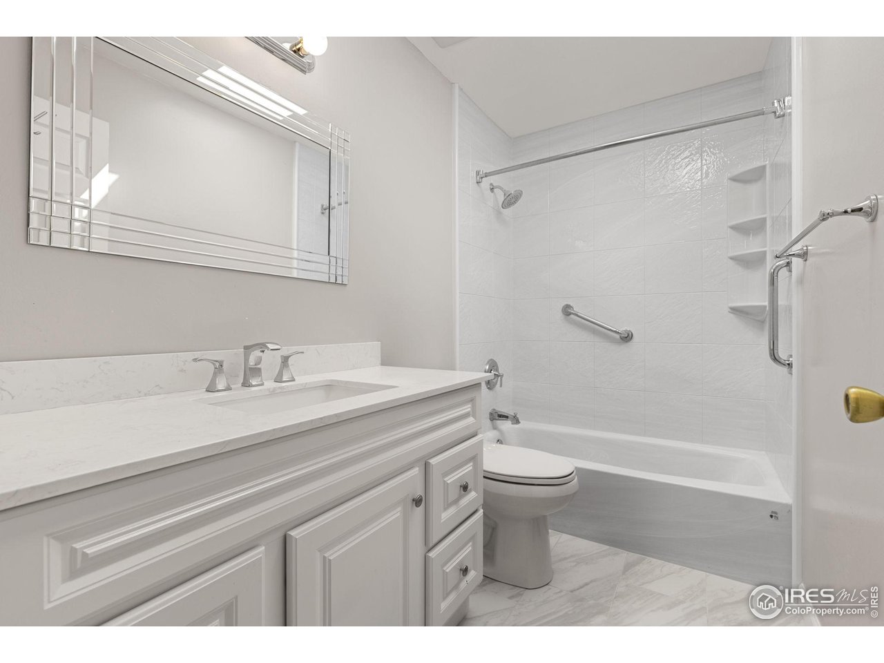Bathroom with a white paneled vanity and a tiled tub-shower with grab bars.