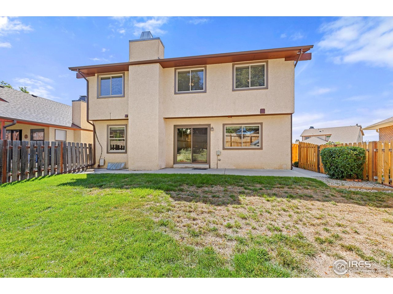 Rear exterior of a two-story stucco house with a fenced backyard and patchy lawn.