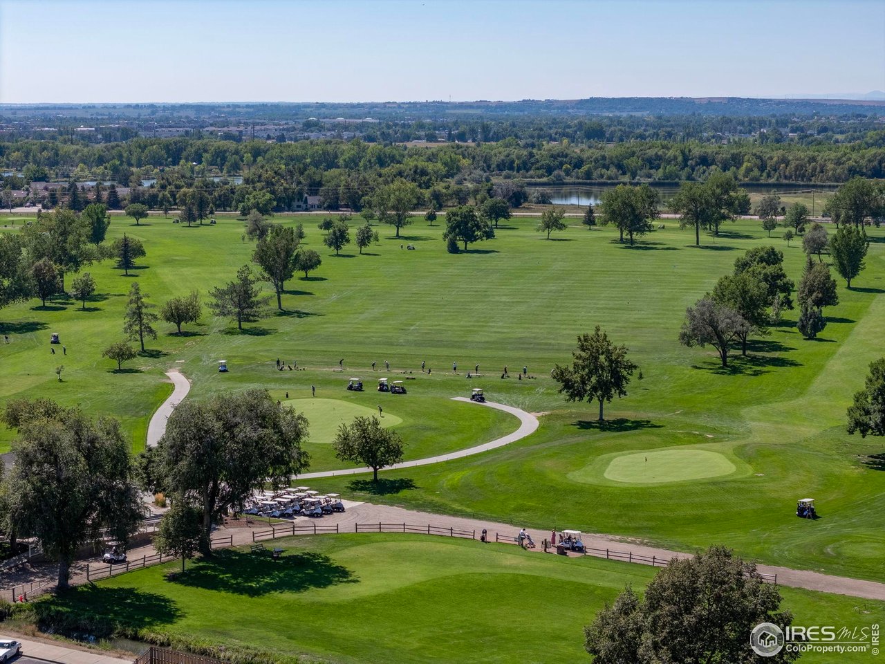 Aerial view of a golf course with rolling greens, golfers, and a pond.