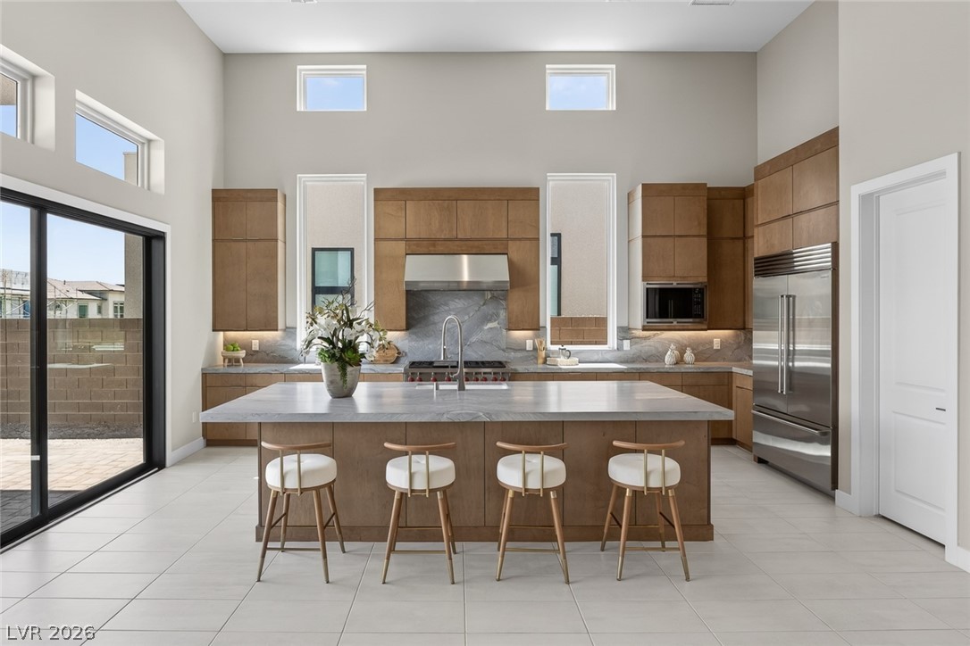 Modern kitchen with a marble island, four stools, warm wood cabinets, and stainless steel appliances.