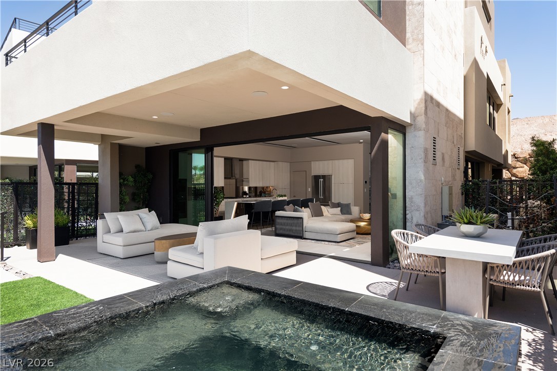 Modern home patio with outdoor lounge seating, open glass doors, and a black-stone spa.