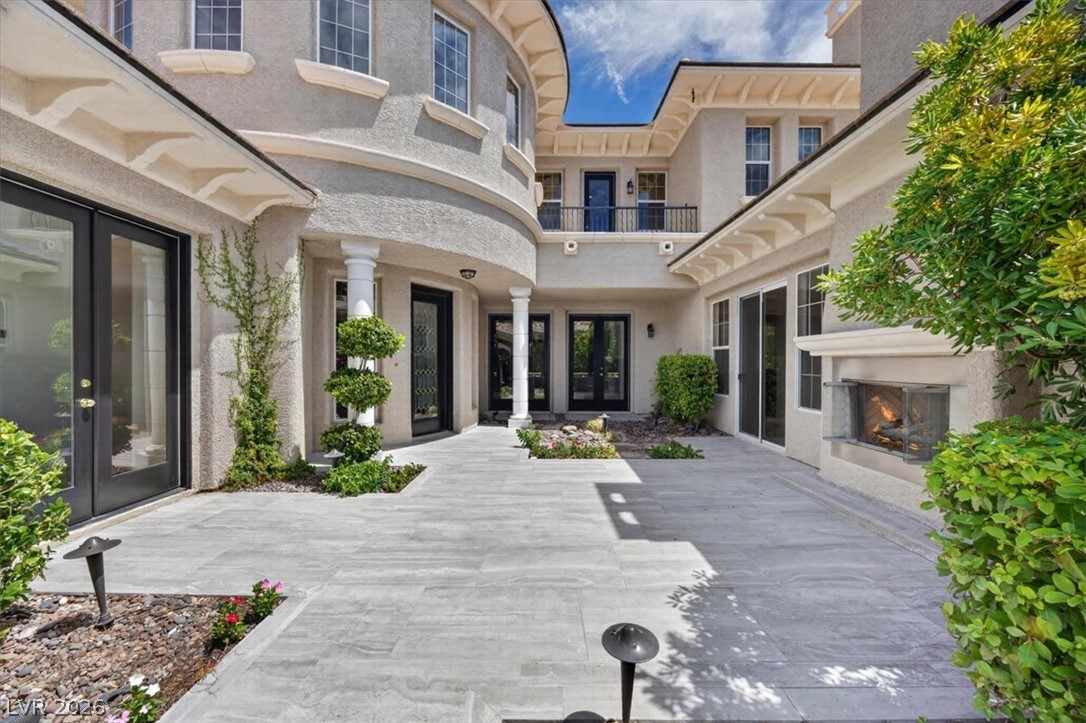Luxury home's stone-paved courtyard with glass doors, landscaped beds, and a built-in outdoor fireplace.