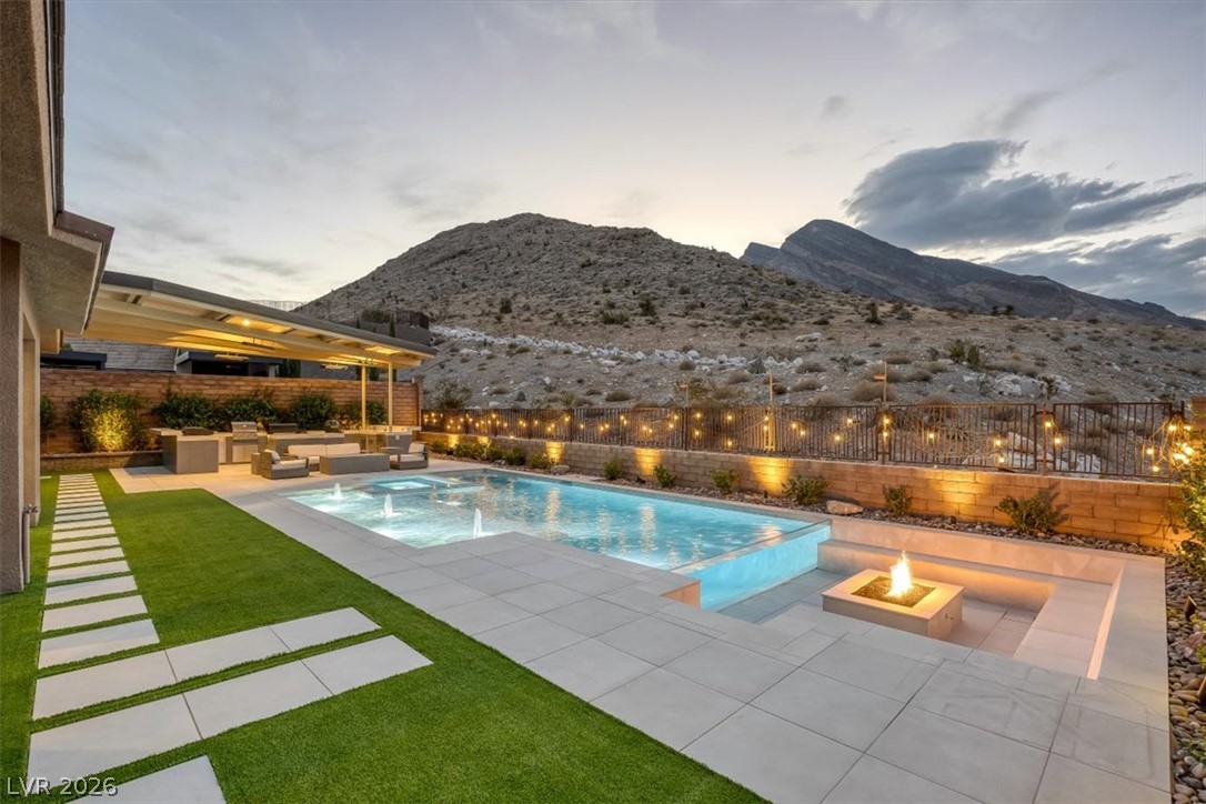 Backyard pool and fire feature beside a covered lounge, with desert mountains beyond.