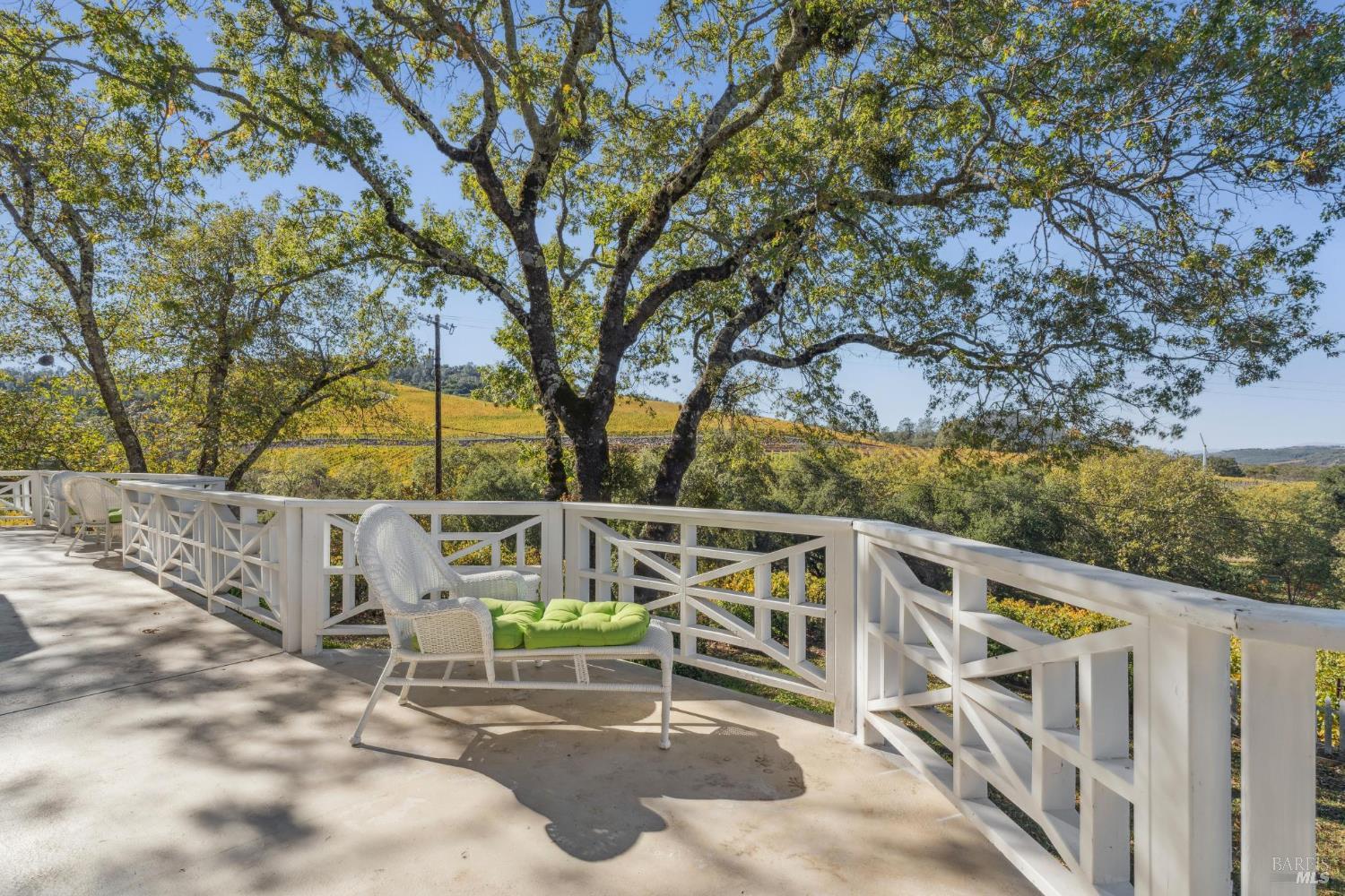 Outdoor deck with white railings and wicker seating overlooking tree-covered golden hills.