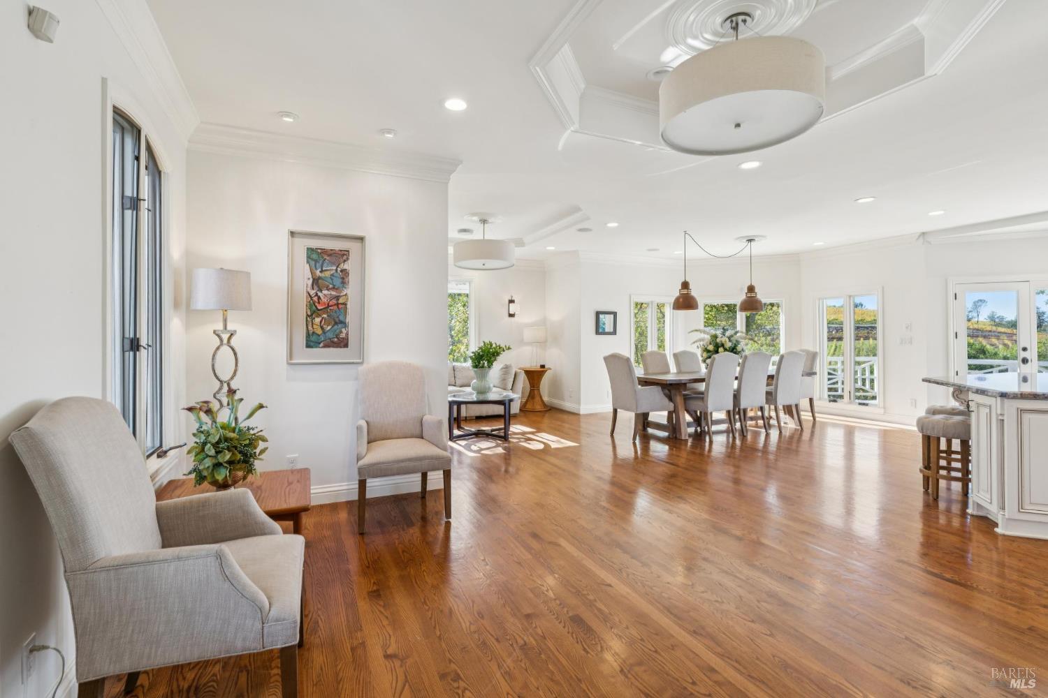 Open-plan living and dining room with hardwood floors and vineyard views through large windows.