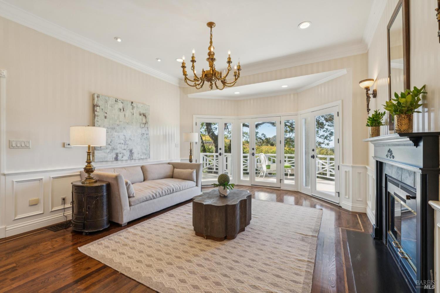 Living room with a gray sofa, brass chandelier, black fireplace, and French doors to a deck.