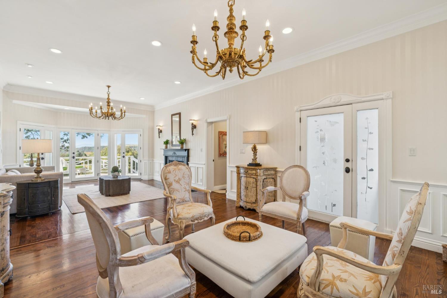 Formal living room with ornate brass chandeliers, cream seating, a fireplace, and glass doors opening to a deck.