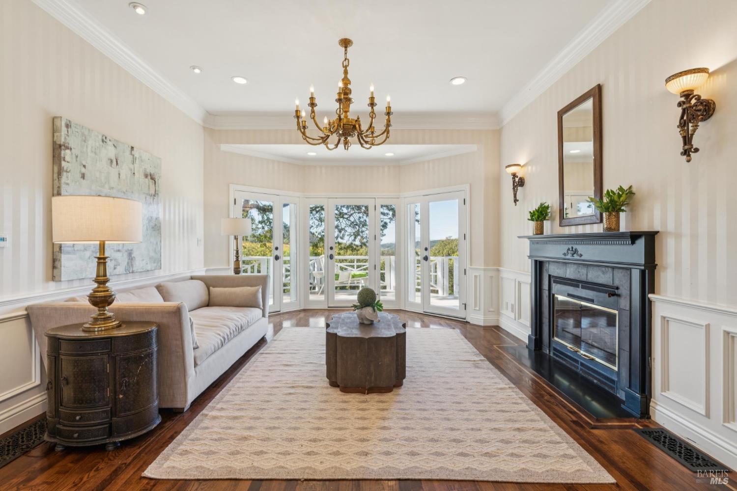 Living room with a dark fireplace, brass chandelier, and glass doors opening onto a deck.
