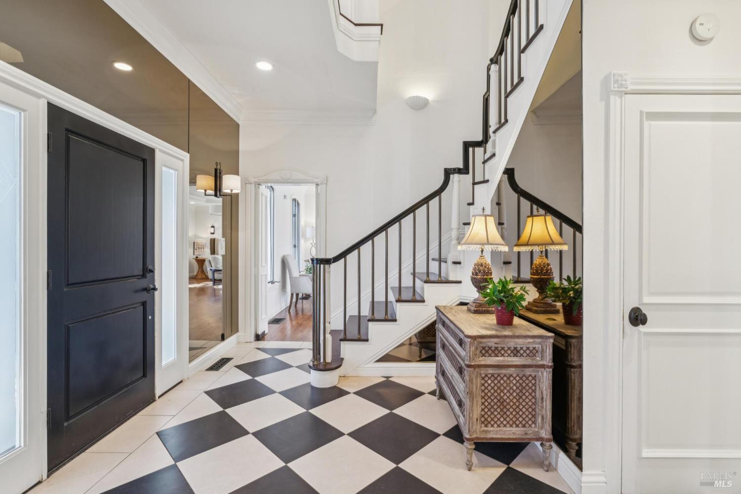 Entry foyer with checkerboard tile, a black front door, and a staircase with dark railings.