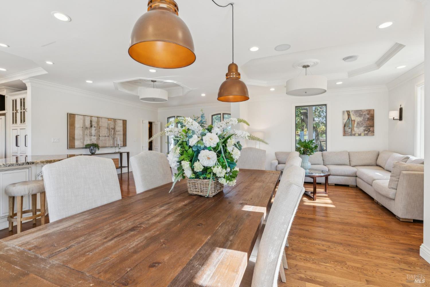 Open-plan dining and living room with a rustic wood table, copper pendant lights, and white sectional sofa.