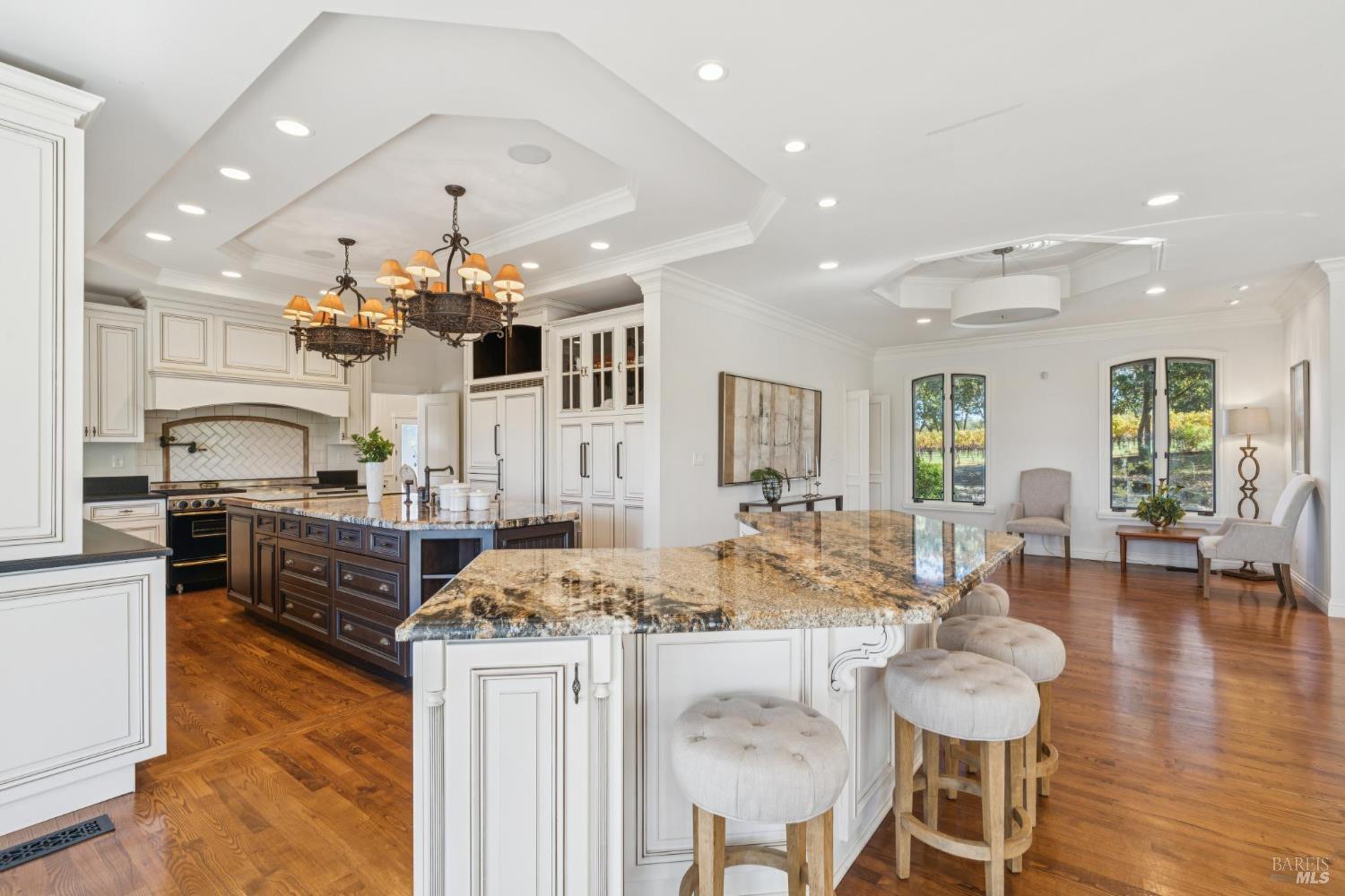 Kitchen with a large granite island, white cabinetry, and a dining area overlooking greenery.