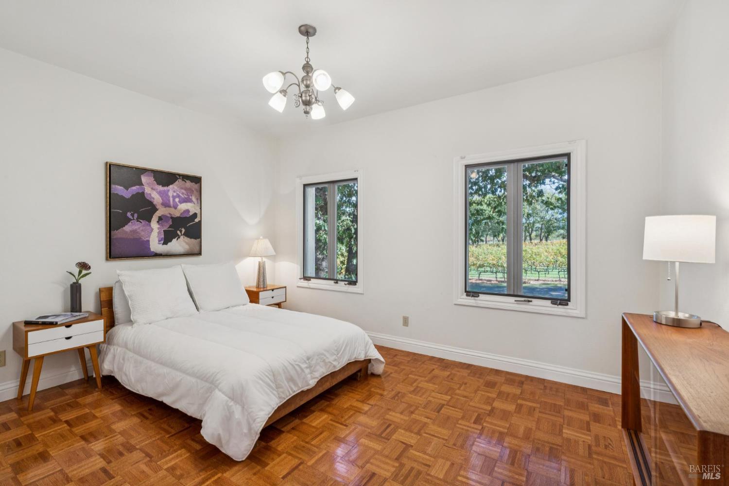 Bedroom with parquet flooring and vineyard views through two windows.