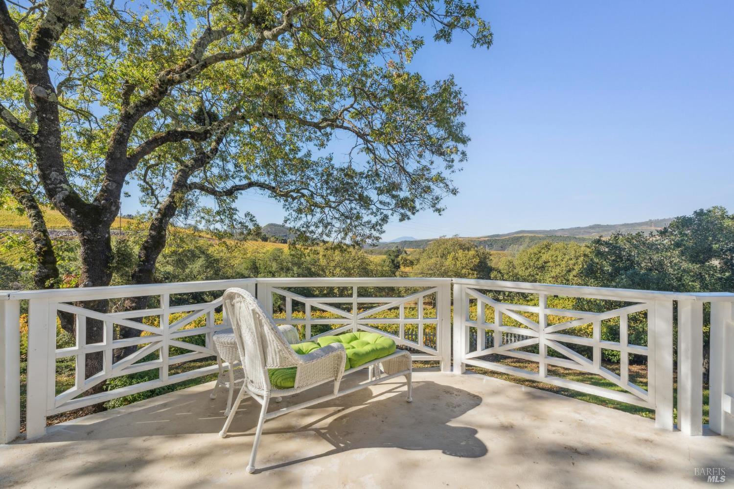 Deck with white railings and a green-cushioned wicker chair overlooking wooded rolling hills.