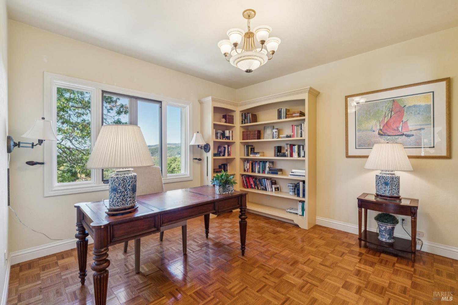 Study with built-in bookshelves, a dark wood desk, and windows overlooking green hills.