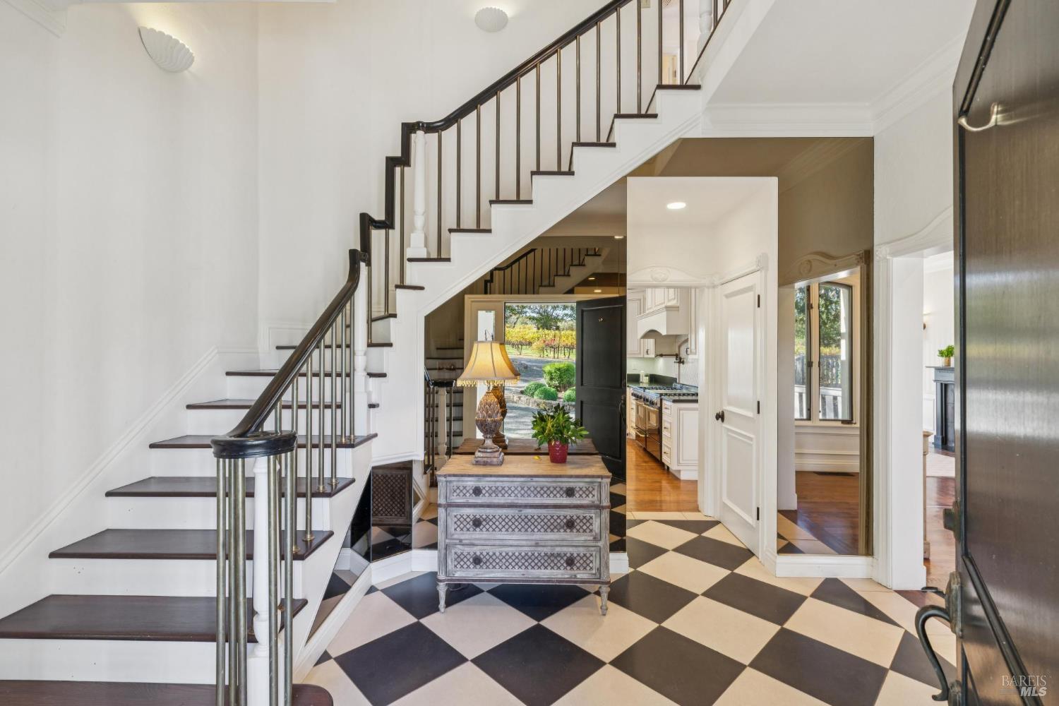Entry foyer with a checkerboard floor, sweeping staircase, and open front door overlooking vineyard rows.