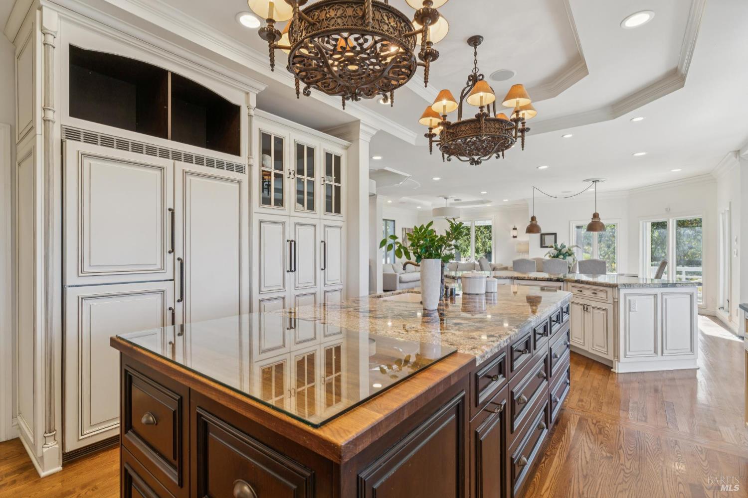 Kitchen with a large dark wood island, cream cabinetry, stone counters, and ornate chandeliers.