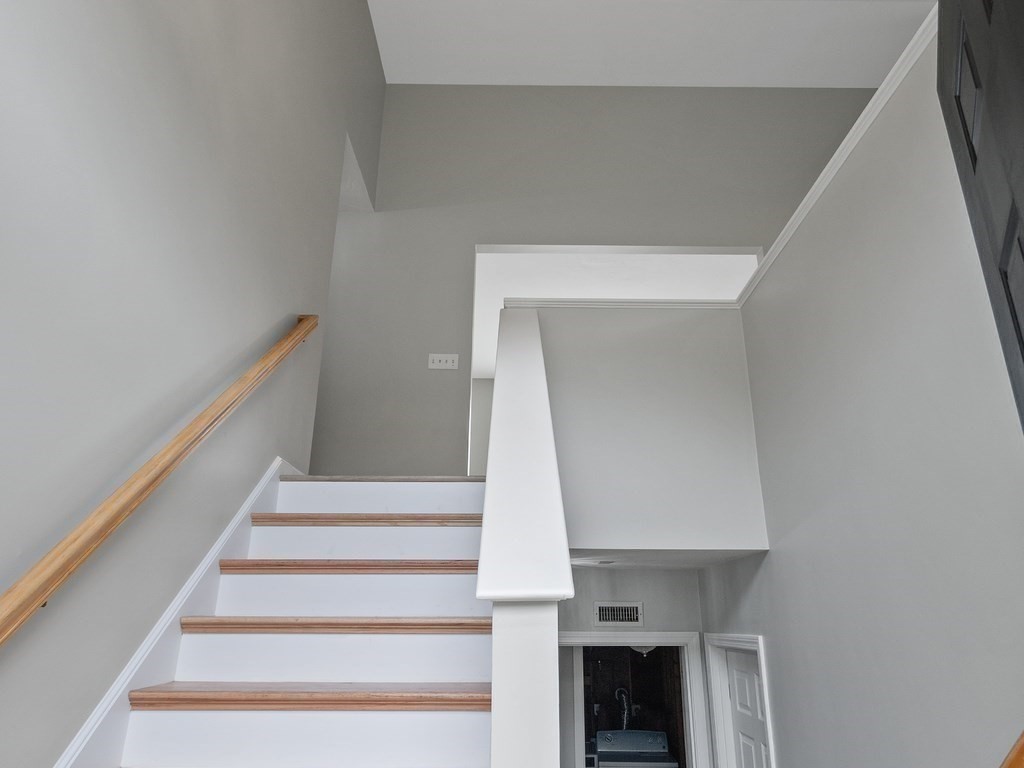Staircase with white risers, wood treads, and a wooden handrail in a gray-walled stairwell.