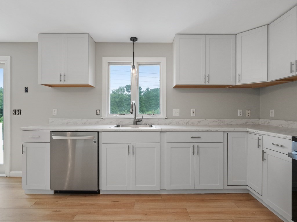 Kitchen with white cabinets, marble-look counters, a stainless dishwasher, and a sink beneath a window.