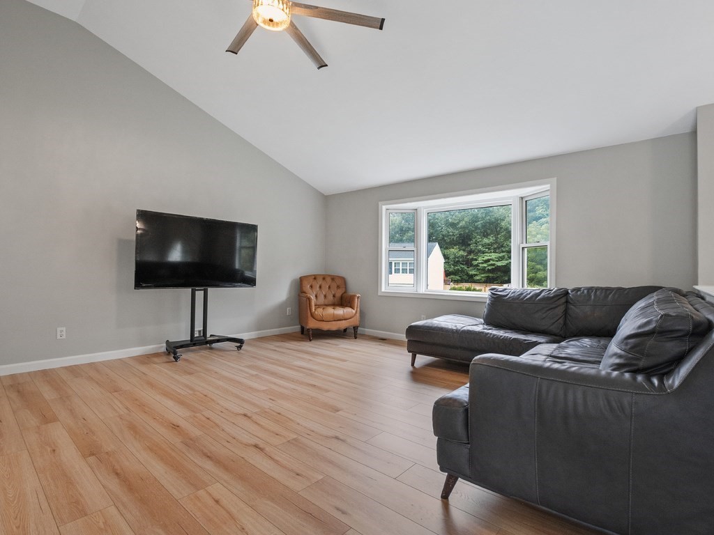 Living room with a black sectional, television, tan armchair, vaulted ceiling, and wide window.