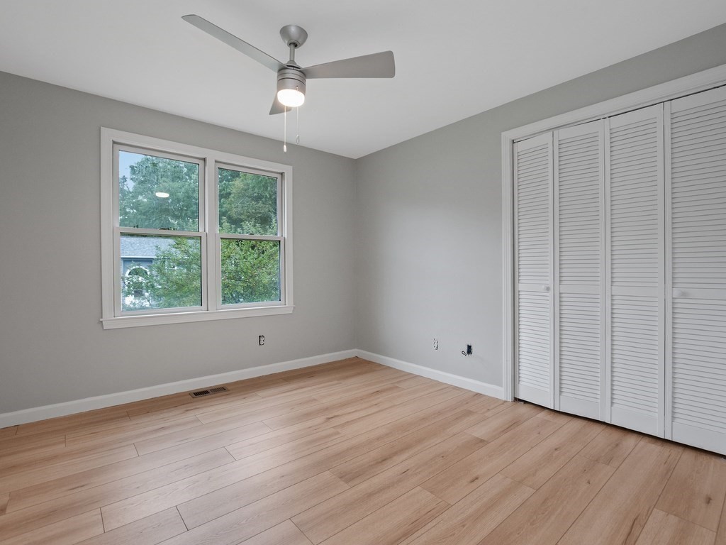 Unfurnished bedroom with wood-look flooring, ceiling fan, double window, and louvered closet doors.