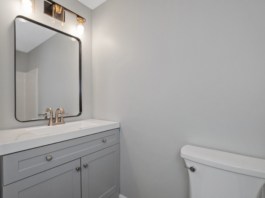 Bathroom vanity with brass faucet and black-framed mirror beside a white toilet.