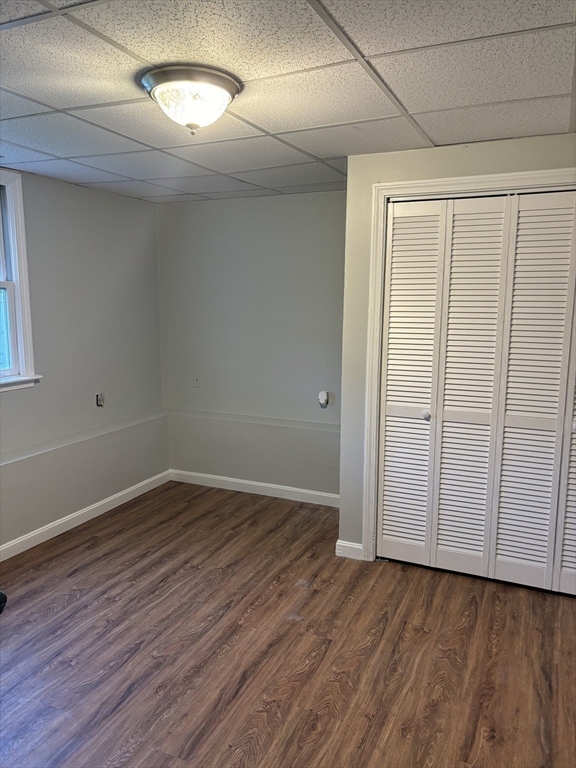 Empty room with wood-look flooring, louvered closet doors, and suspended ceiling.