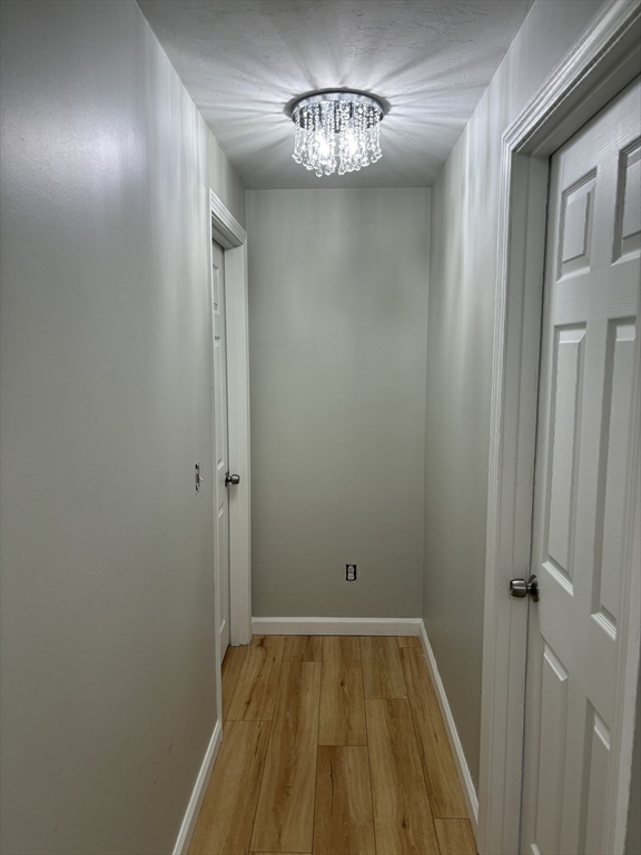 Unfurnished hallway with wood-look flooring and a crystal chandelier.