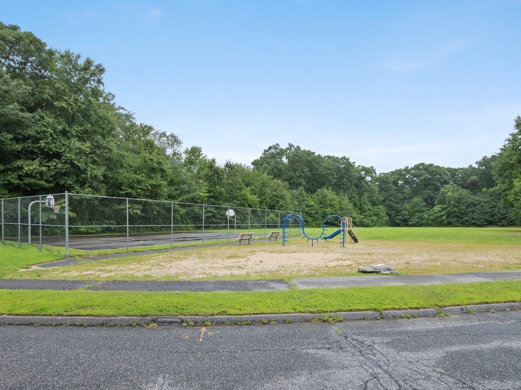 Recreation area with a blue playground structure and fenced basketball court among mature trees.